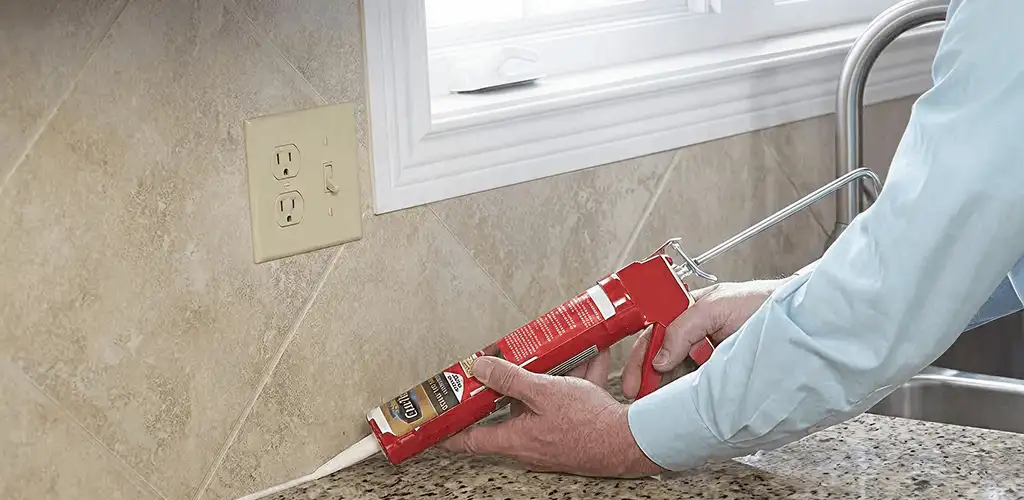 Handyman applying caulk along a kitchen backsplash and countertop seam in Newark, NJ