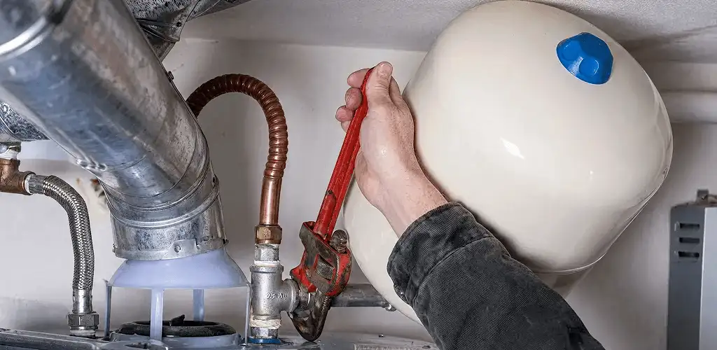 Water heater repair technician tightening plumbing connections near a tank unit in Newark, NJ